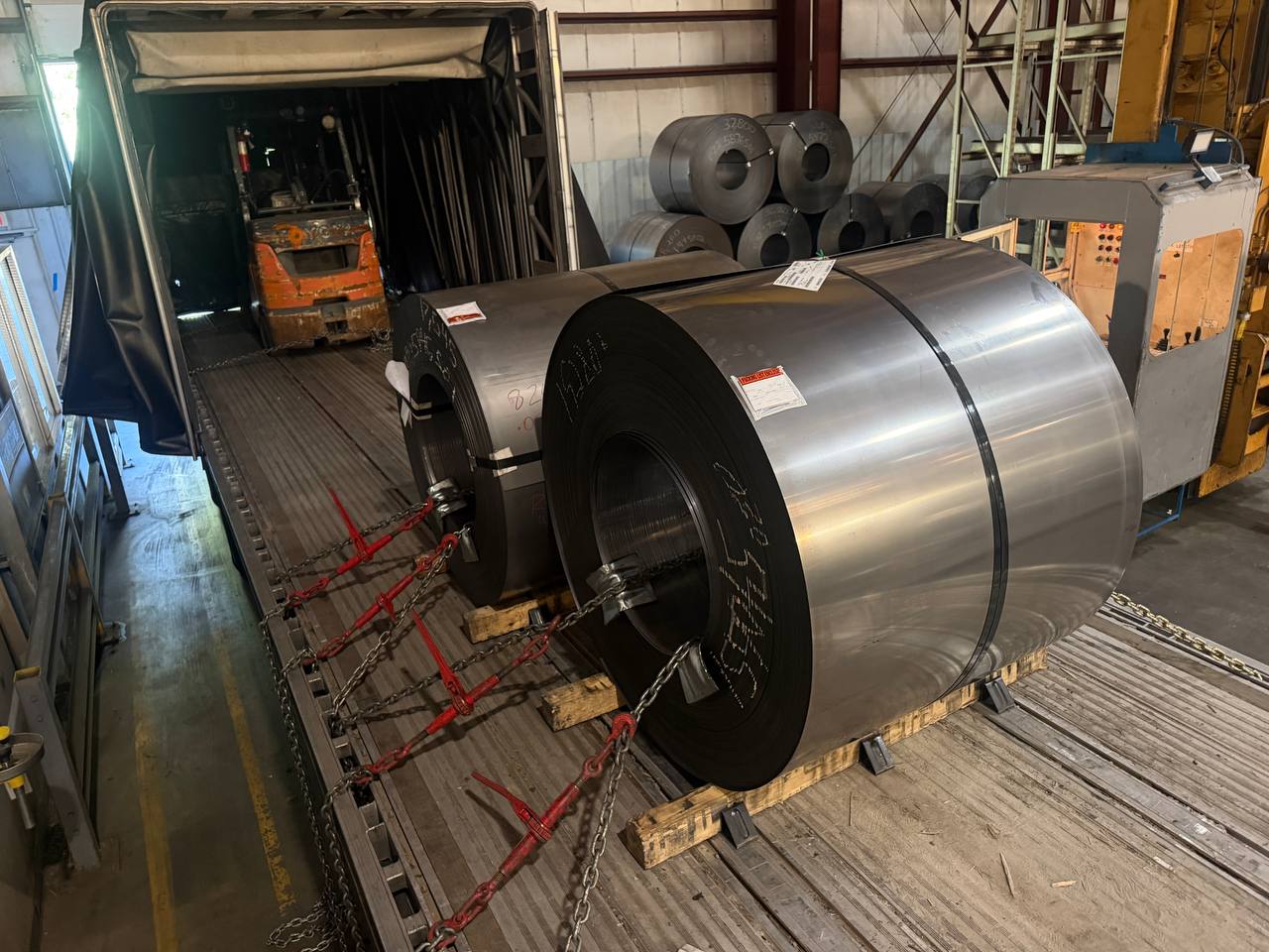 Steel coils being loaded by forklift into a Conestoga trailer